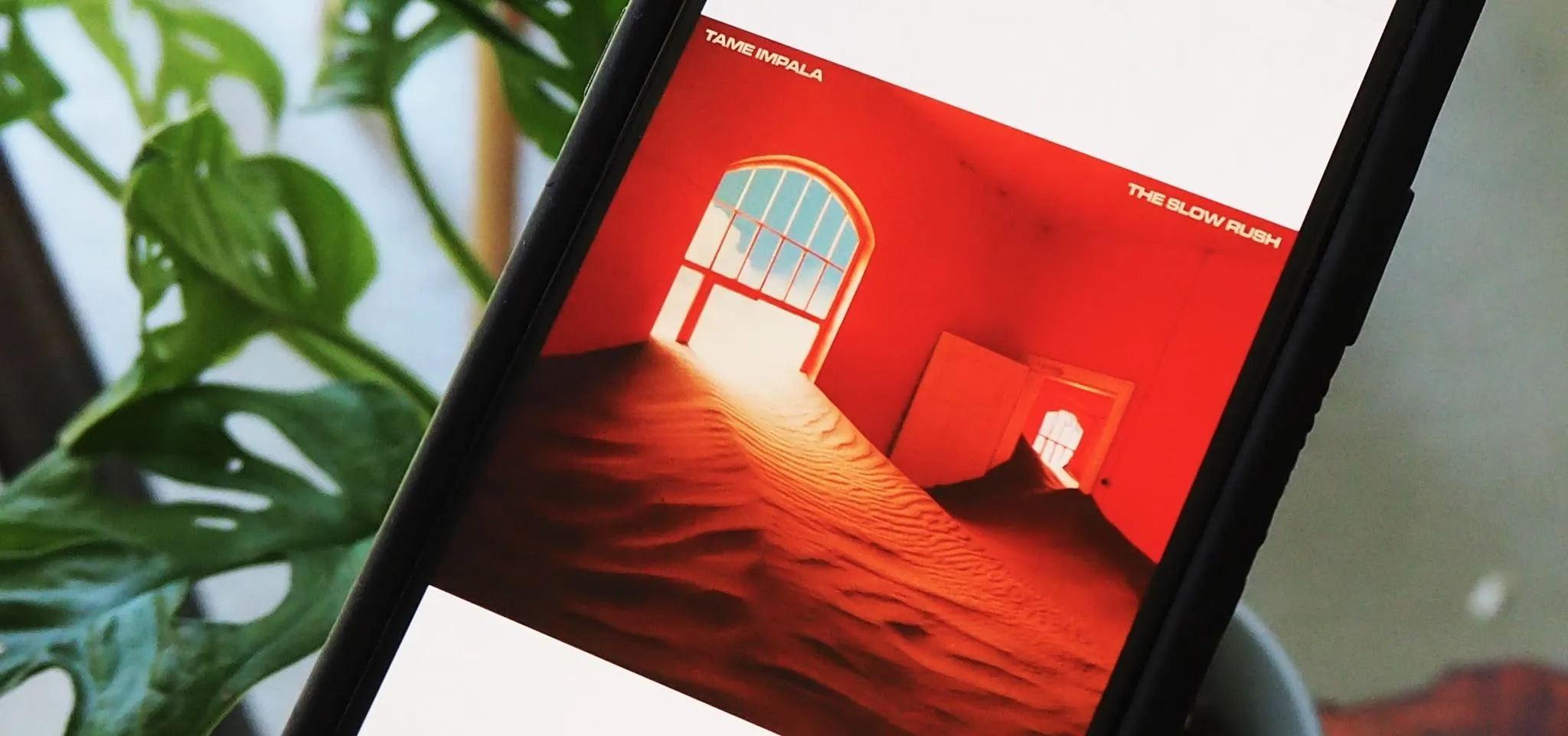 A smartphone displaying an artistic red-themed image with a window and a sandy landscape.