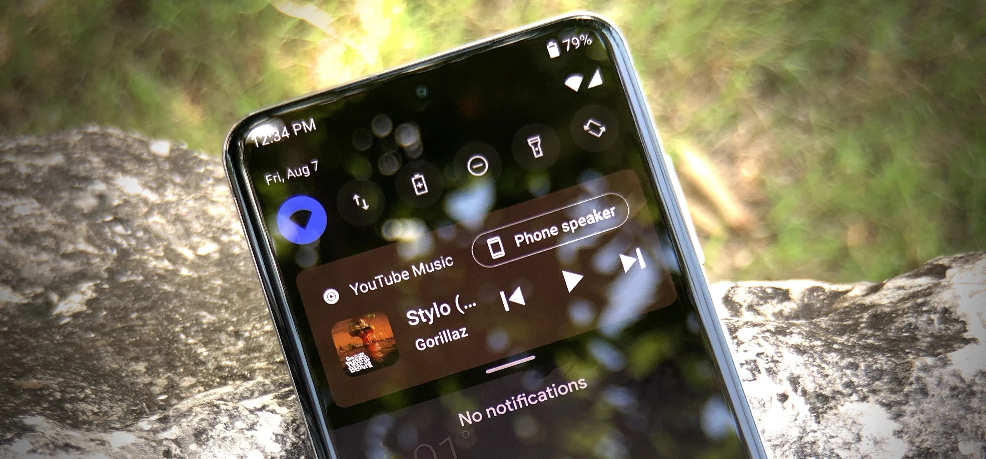 Smartphone displaying music playback controls with outdoor background.