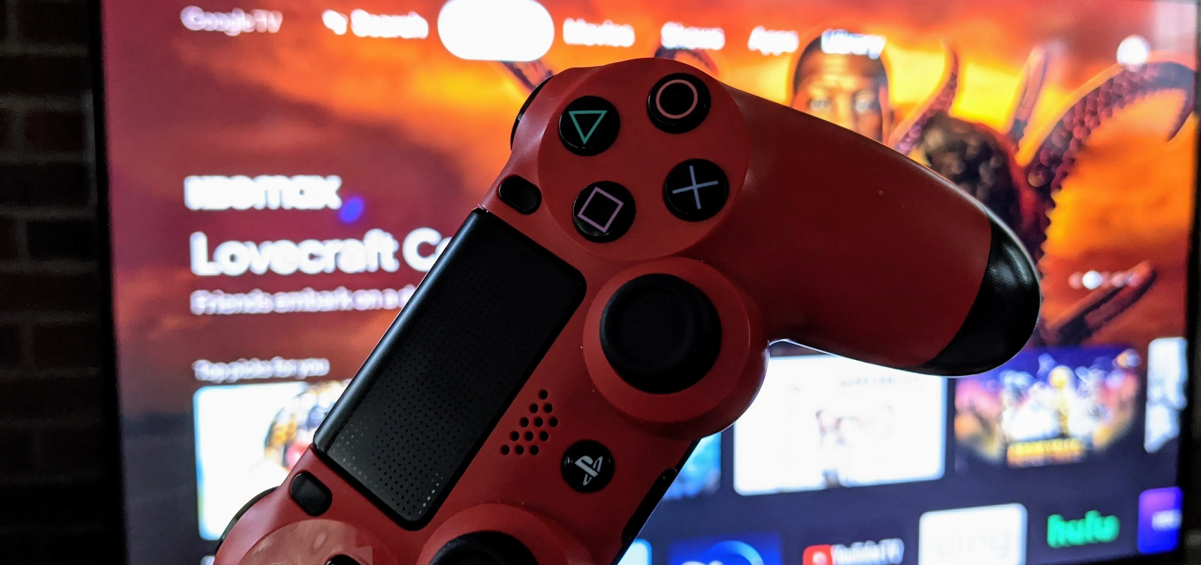 Red PlayStation 4 controller in front of a TV displaying a gaming interface.