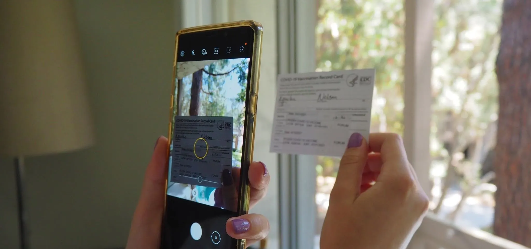 Person holding a smartphone and a card near a window.