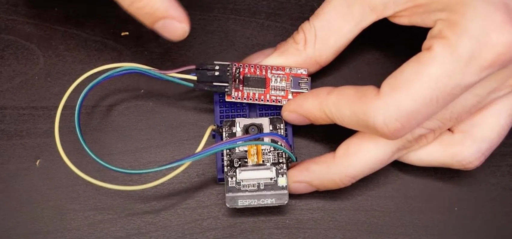 Hands connecting wires to an electronic circuit board.