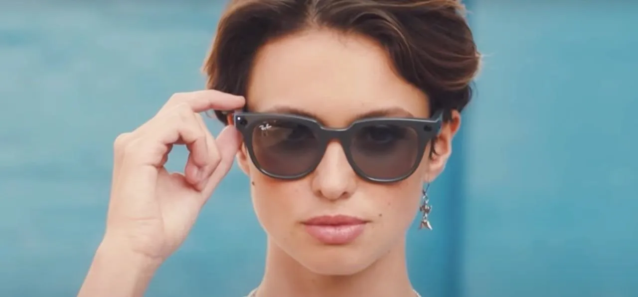 Woman adjusting sunglasses against a blue background.
