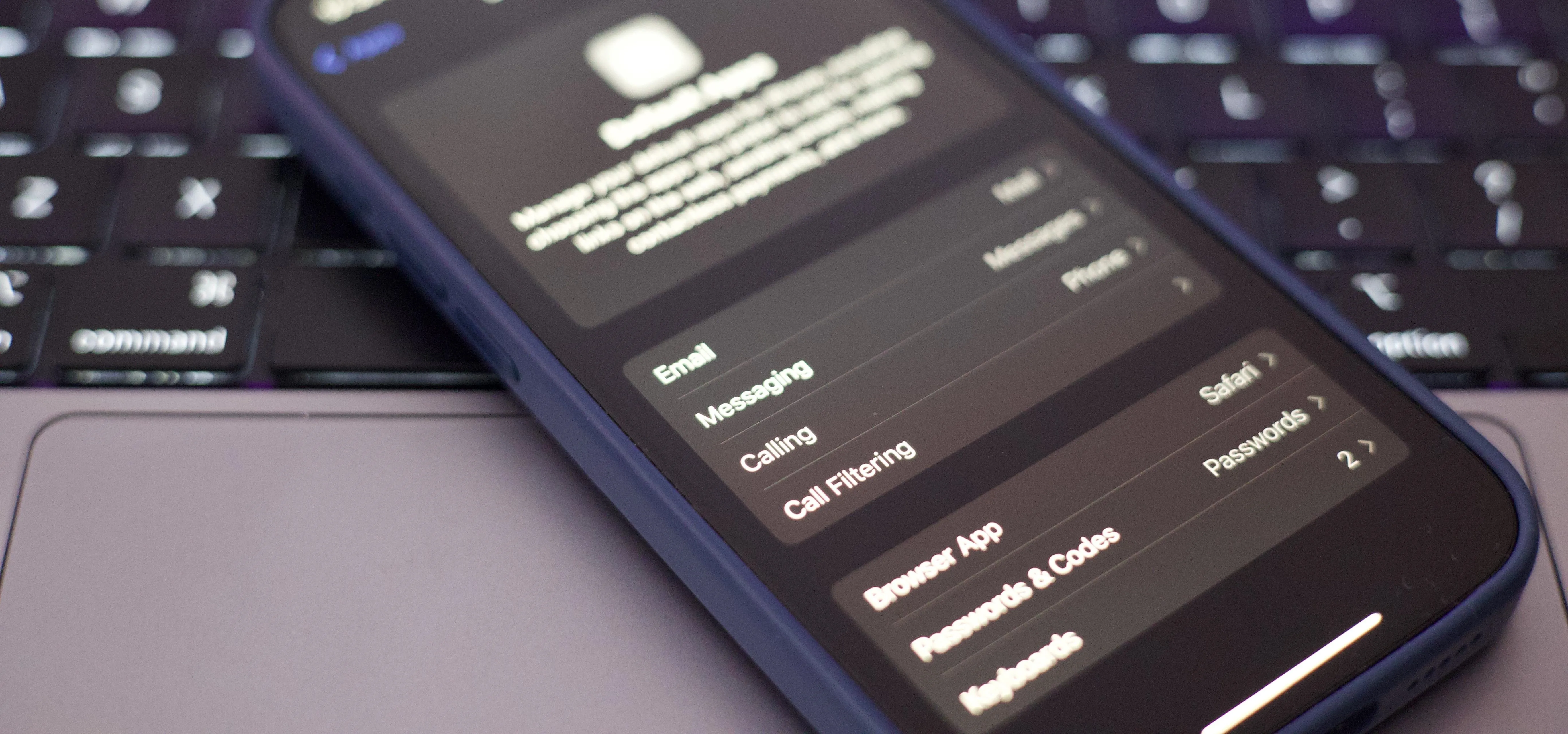 Smartphone displaying settings on dark mode next to a laptop keyboard.